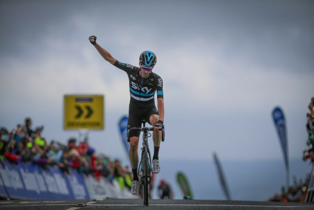 Rider wearing Sky jersey raising one arm as he crosses the finish line